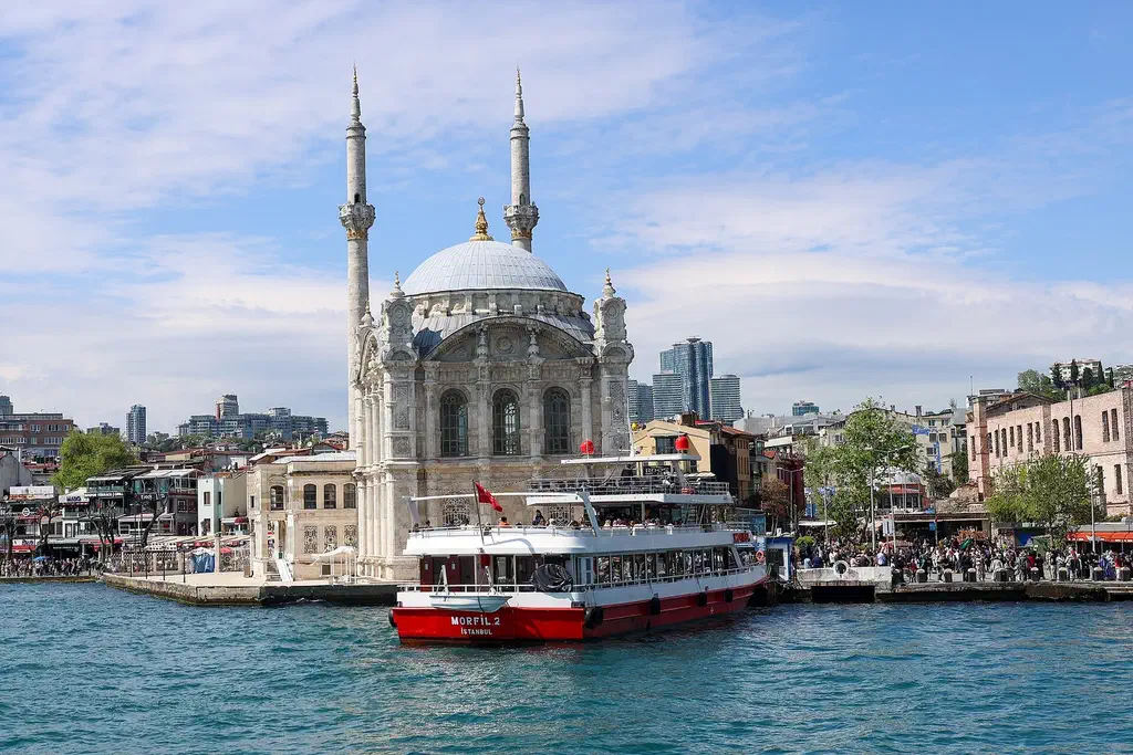 Ortakoy Mosque on the Bosphorus waterfront with a ferry passing and the lively Ortakoy square behind it